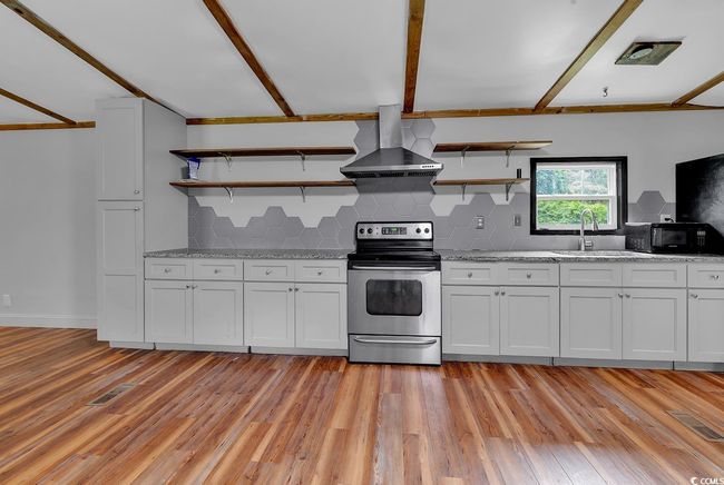 Kitchen featuring stainless steel appliances, wall chimney range hood, open shelves, light wood-type flooring, and backsplash | Image 5
