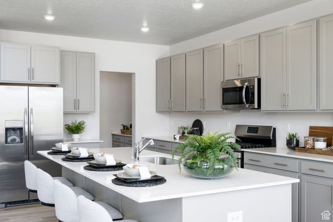 Kitchen with appliances with stainless steel finishes, gray cabinetry, a sink, a center island with sink, and light countertops | Image 4