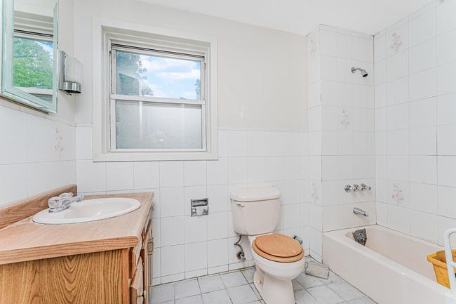 Bathroom with vanity, tile patterned floors, tub / shower combination, a wainscoted wall, and tile walls | Image 17
