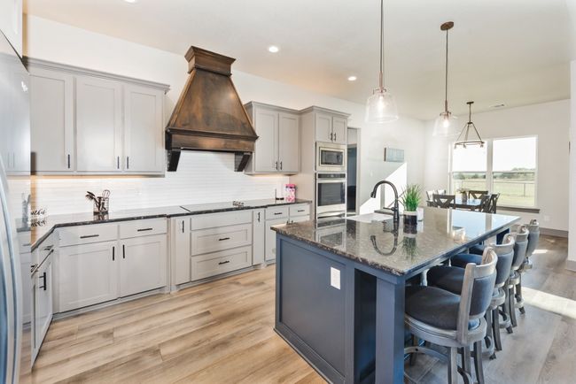 Kitchen with backsplash, custom range hood, dark stone countertops, a breakfast bar, and stainless steel appliances | Image 8