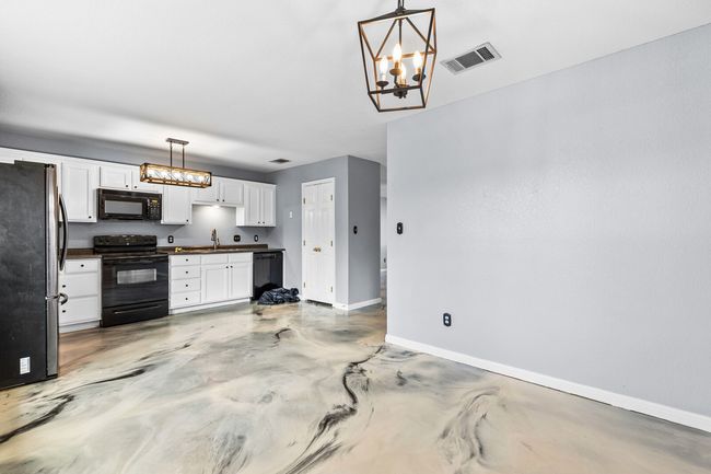 Kitchen featuring a chandelier, dark countertops, black appliances, and white cabinetry | Image 22