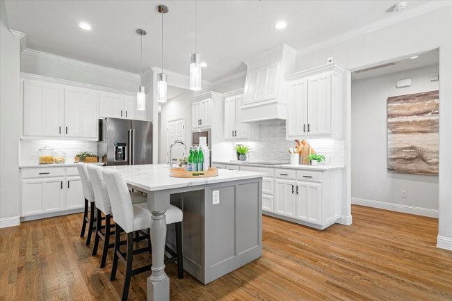 Kitchen with stainless steel fridge, a kitchen bar, decorative backsplash, white cabinets, and an island with sink | Image 9