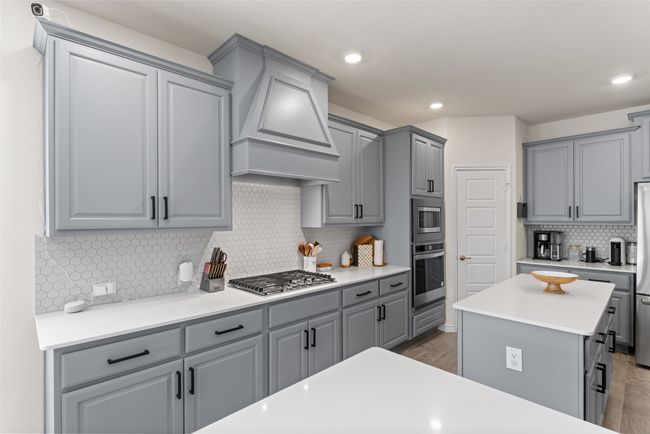 Kitchen with gray cabinets, appliances with stainless steel finishes, backsplash, custom exhaust hood, and wood finished floors | Image 6