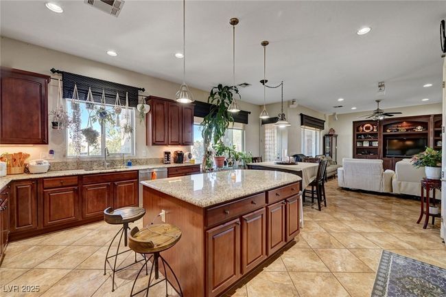 Kitchen featuring recessed lighting, light tile patterned floors, a center island, light stone countertops, and decorative light fixtures | Image 16