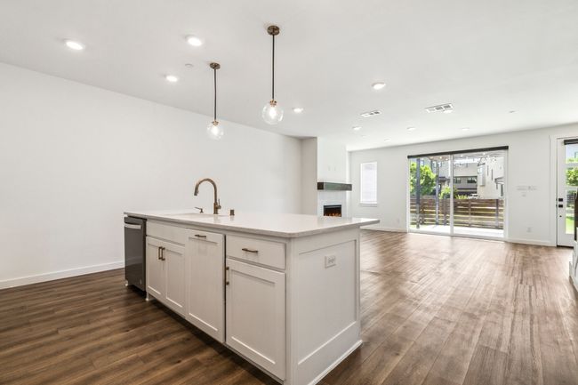 Kitchen with a sink, dishwasher, dark wood finished floors, open floor plan, and a warm lit fireplace | Image 12