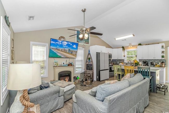 Living room featuring lofted ceiling, a ceiling fan, light wood-type flooring, and a warm lit fireplace | Image 4