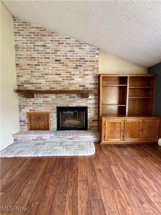 Unfurnished living room featuring hardwood / wood-style floors, a textured ceiling, lofted ceiling, and a brick fireplace | Image 13