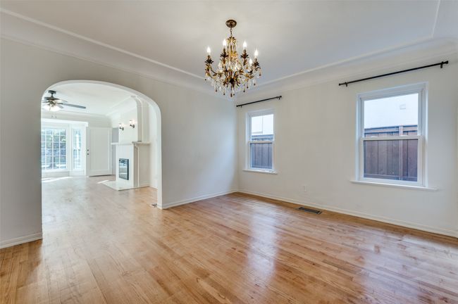 Empty room with arched walkways, light wood finished floors, a chandelier, plenty of natural light, and crown molding | Image 10