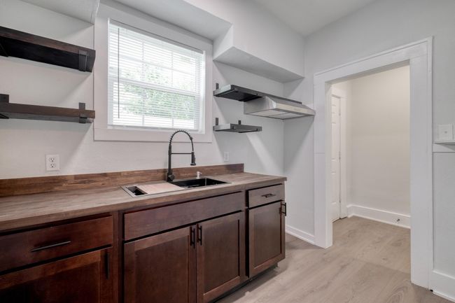 Kitchen with open shelves, butcher block counters, light wood finished floors, and dark brown cabinets | Image 5