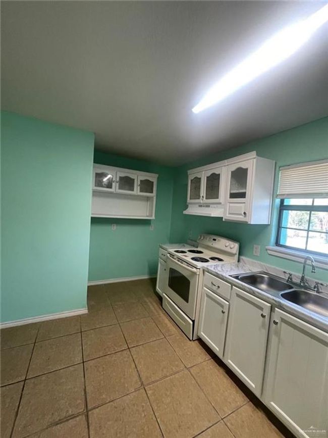 Kitchen with white range with electric cooktop, white cabinets, extractor fan, and a sink | Image 5
