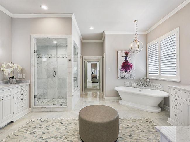 Bathroom featuring crown molding, a freestanding tub, a stall shower, a chandelier, and marble look tile flooring | Image 22