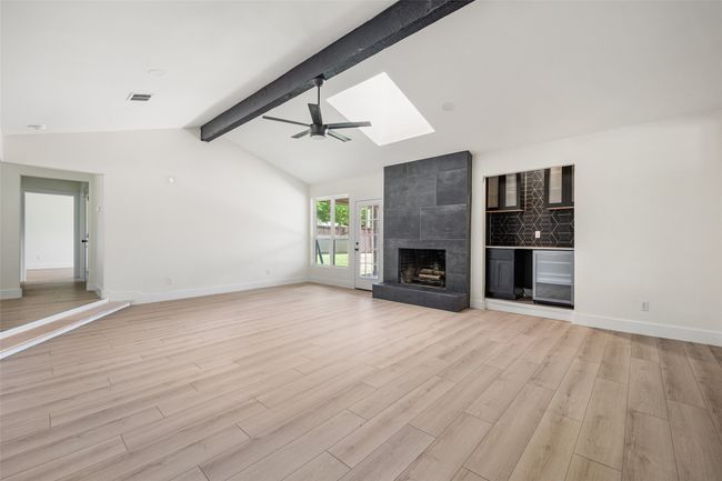Unfurnished living room featuring light wood-style flooring, ceiling fan, a skylight, and a fireplace | Image 6