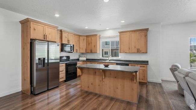 Kitchen with black appliances, dark countertops, dark wood-style floors, a center island, and recessed lighting | Image 9