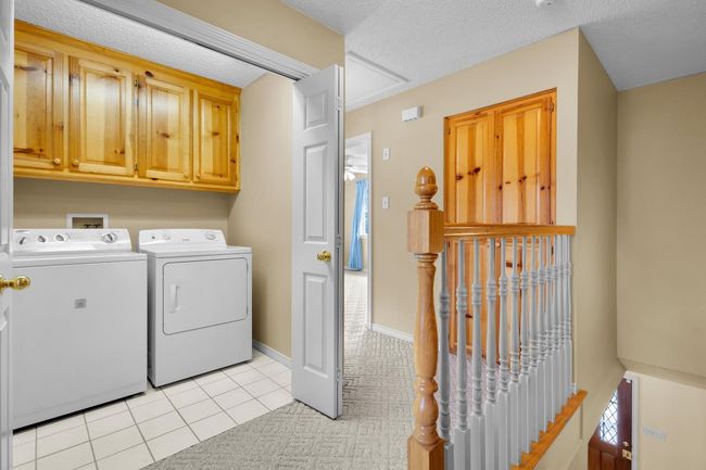 Second Floor laundry area featuring separate washer and dryer, cabinet space, light tile patterned floors, and light colored carpet | Image 21
