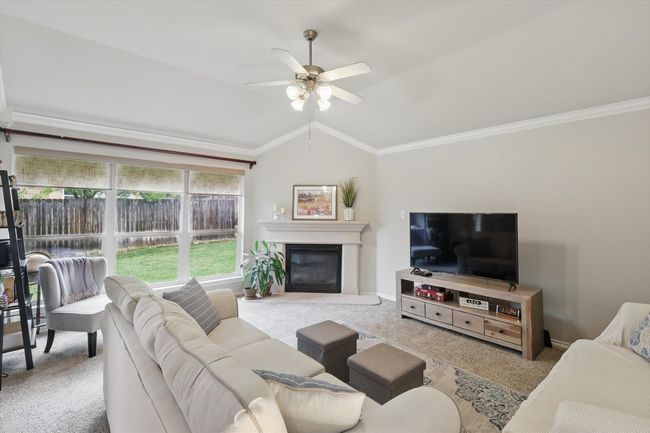 Living room with a ceiling fan, crown molding, carpet floors, lofted ceiling, and a glass covered fireplace | Image 19