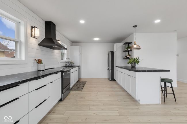 kitchen featuring exhaust hood, a kitchen breakfast bar, light wood finished floors, white cabinetry, and stainless steel appliances | Image 26