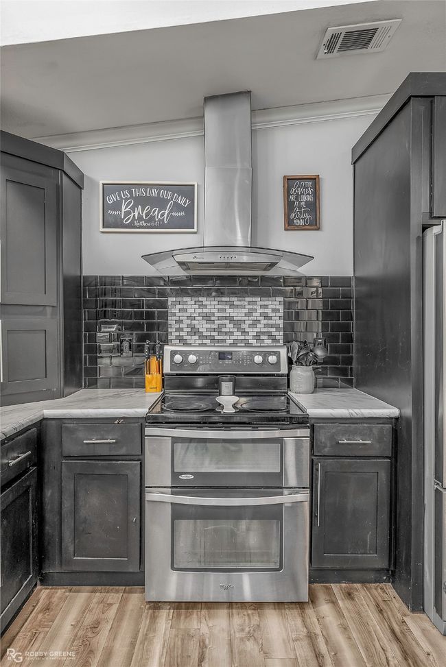 Kitchen with island exhaust hood, range with two ovens, visible vents, backsplash, and light countertops | Image 21