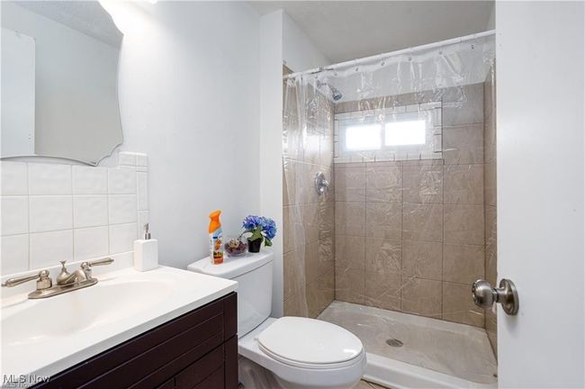 Full bathroom featuring backsplash, a tile shower, vanity, and toilet | Image 14