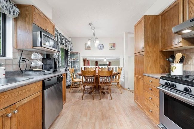 Kitchen with under cabinet range hood, light wood-type flooring, decorative backsplash, brown cabinetry, and stainless steel appliances | Image 12