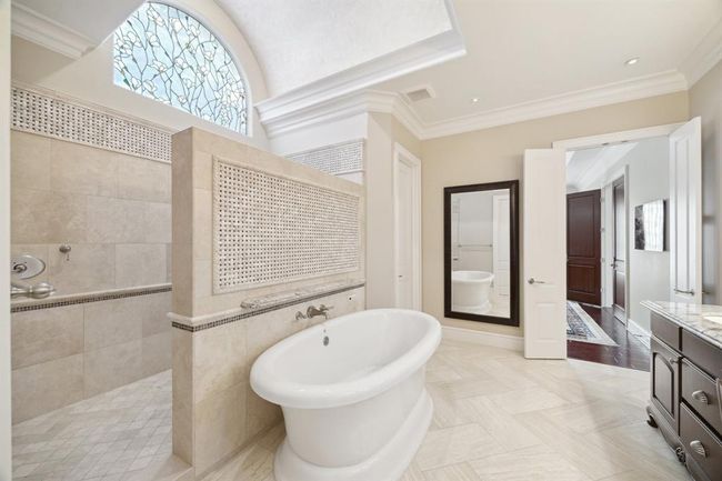 This luxurious bathroom features a spacious layout with a central freestanding tub, elegant tile flooring, and a large walk-in shower. A decorative stained glass window adds charm, while ample natural light enhances the airy feel. | Image 22