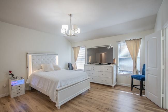 Bedroom with baseboards, a notable chandelier, light wood finished floors, and lofted ceiling | Image 11