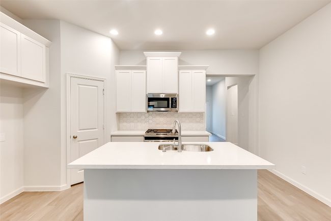 Kitchen with stainless steel appliances, a sink, light wood-style floors, backsplash, and white cabinetry | Image 10