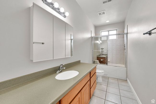 Full bath with toilet, visible vents, shower / bath combination with glass door, tile patterned flooring, and vanity | Image 38