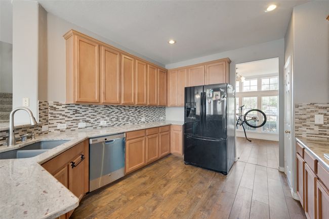 Kitchen featuring freestanding refrigerator, light stone countertops, dishwasher, hardwood / wood-style flooring, and a sink | Image 11