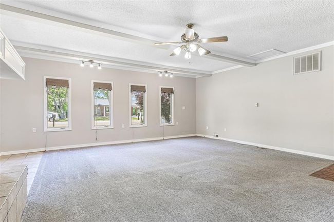 Carpeted empty room featuring a textured ceiling, attic access, ceiling fan, beam ceiling, and baseboards | Image 44