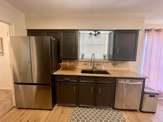 Kitchen featuring stainless steel appliances, light wood finished floors, crown molding, a sink, and light stone countertops | Image 8