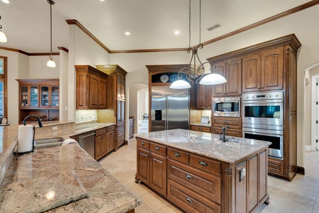 Kitchen featuring arched walkways, ornamental molding, tasteful backsplash, an island with sink, and light stone counters | Image 13