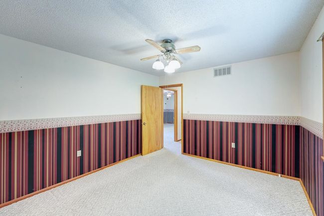 Carpeted empty room with wainscoting, a ceiling fan, and a textured ceiling | Image 13