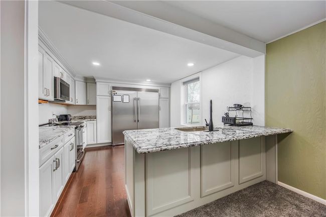 Kitchen with light stone countertops, a peninsula, stainless steel appliances, and a sink | Image 31