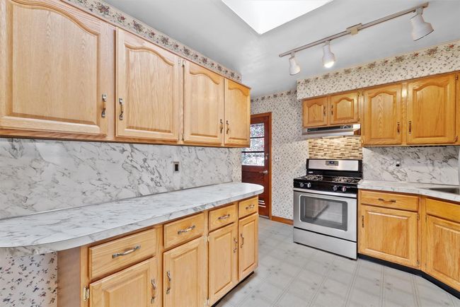 Kitchen with light floors, light countertops, under cabinet range hood, stainless steel gas range oven, and wallpapered walls | Image 13