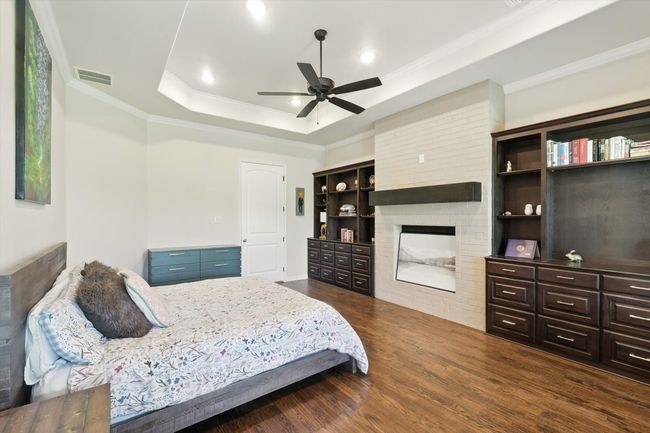 Bedroom with a fireplace, a tray ceiling, dark wood-style flooring, ornamental molding, and ceiling fan | Image 20