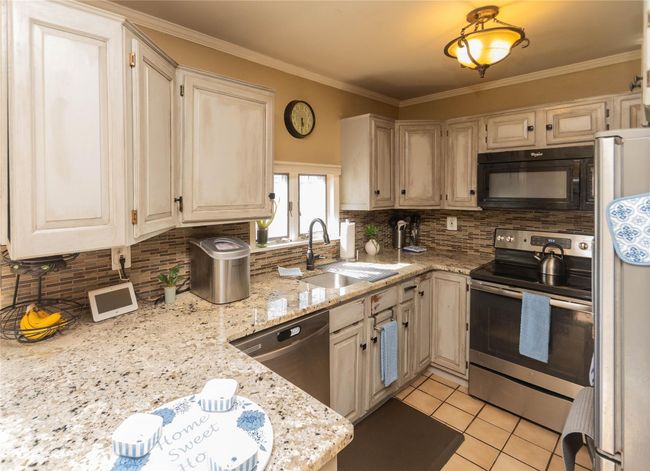 Kitchen featuring a sink, decorative backsplash, light tile patterned flooring, stainless steel appliances, and light stone countertops | Image 11