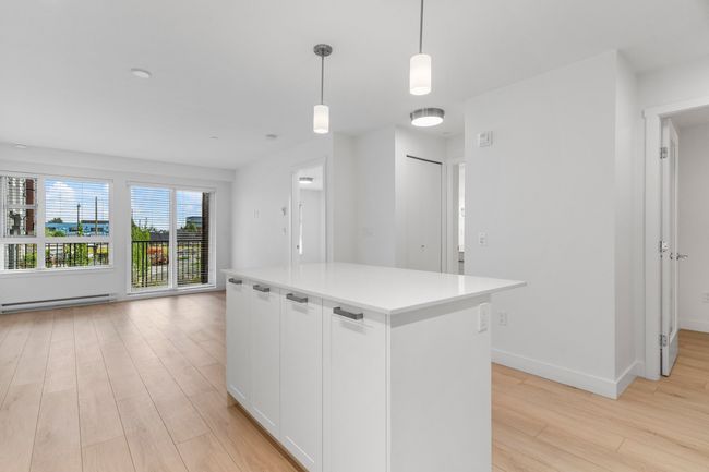 Kitchen featuring a baseboard radiator, light wood finished floors, white cabinetry, light countertops, and pendant lighting | Image 6