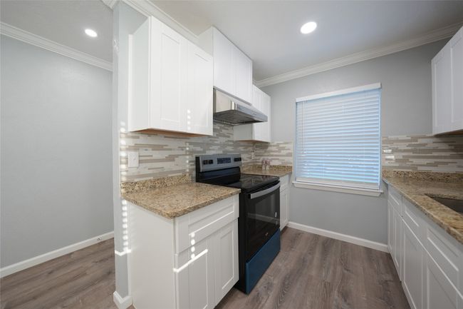 Kitchen with range with electric cooktop, decorative backsplash, white cabinets, dark wood-style floors, and under cabinet range hood | Image 4