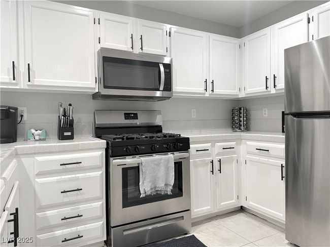Kitchen featuring light tile patterned flooring, white cabinetry, stainless steel appliances, and light countertops | Image 14
