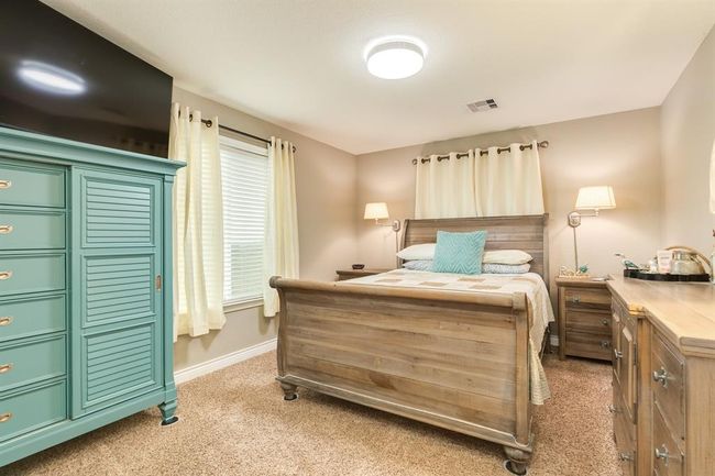 The 2nd bedroom with warm tones featuring a wooden bed, teal chest of drawers, and beige carpet. Bright natural light filters through light curtains, complemented by modern lighting fixtures and closet. | Image 17