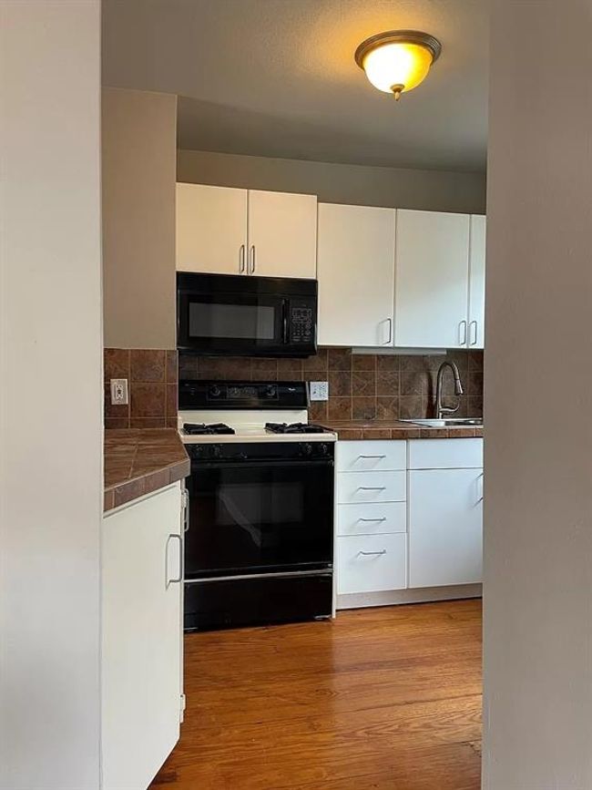 Kitchen with gas stove, black microwave, white cabinetry, and backsplash | Image 5