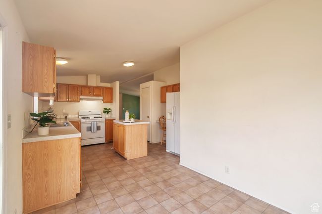 Kitchen with white appliances, light countertops, a center island, under cabinet range hood, and a sink | Image 6