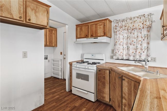 Kitchen with dark wood-type flooring, light countertops, white gas stove, under cabinet range hood, and a sink | Image 14