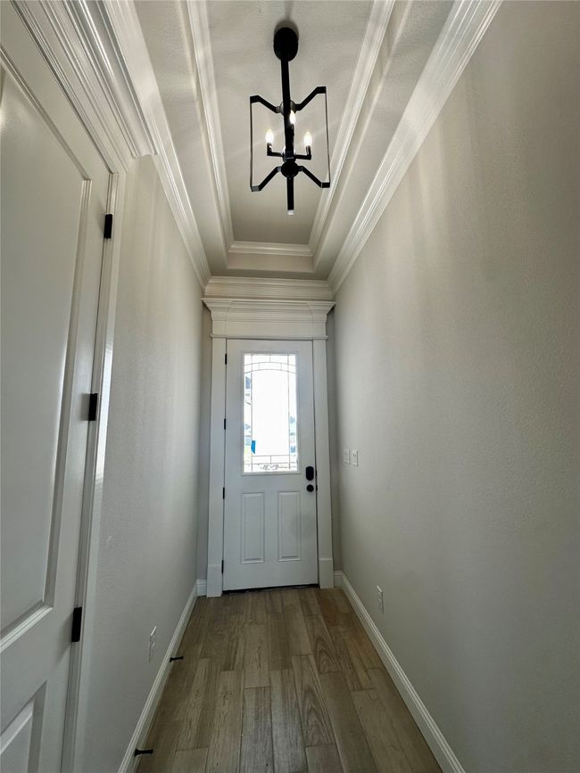 Doorway to outside with wood finished floors, a chandelier, crown molding, baseboards, and a raised ceiling | Image 4