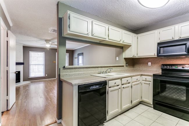 Kitchen featuring black appliances, a textured ceiling, ceiling fan, light countertops, and a fireplace | Image 11