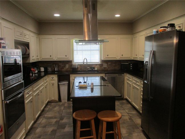 Kitchen featuring tasteful backsplash, stainless steel appliances, dark tile patterned flooring, ventilation hood, and a center island | Image 16