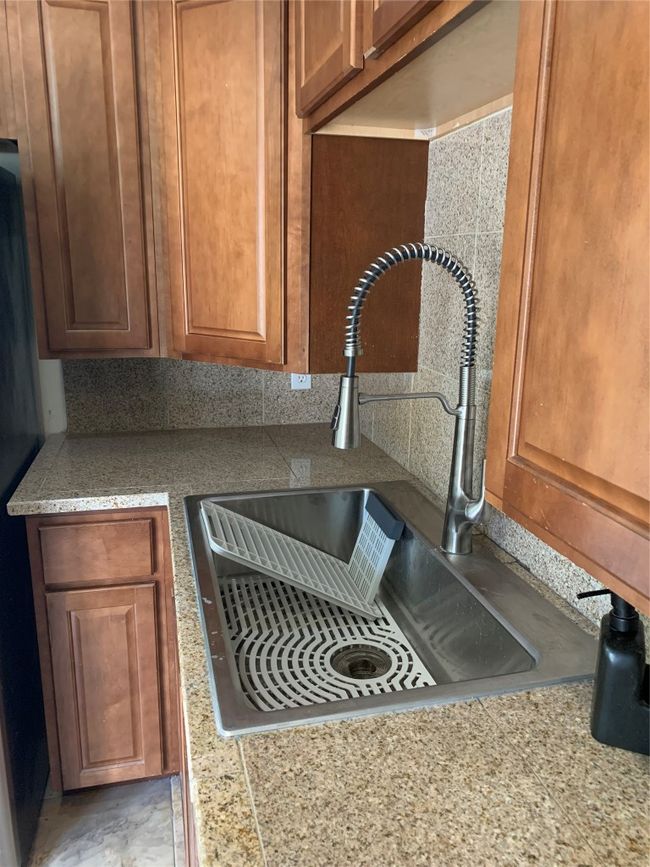 Kitchen view of a sink, light countertops, backsplash, and brown cabinets | Image 8