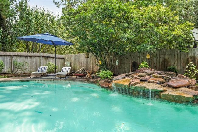 This backyard features a serene pool with a rock waterfall, surrounded by lush greenery offering a peaceful outdoor retreat. | Image 10
