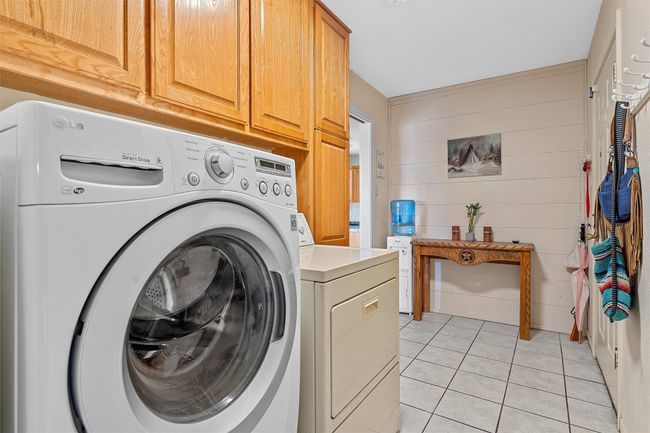 Washroom featuring cabinet space, wooden walls, washing machine and clothes dryer, and light tile patterned flooring | Image 15