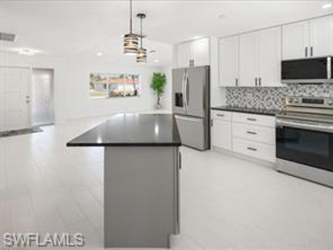 Kitchen with light hardwood / wood-style floors, stainless steel appliances, backsplash, white cabinets, and pendant lighting | Image 5